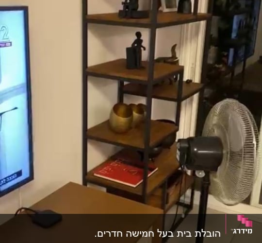 מאוורר עומד ליד מדף עם חפצים דקורטיביים